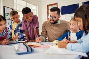 Elementary school students gather around their teacher as he guides them through a writing assignment.